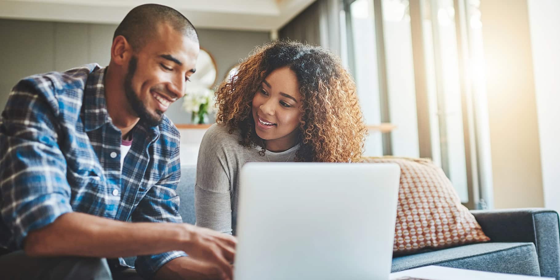 A young couple sitting on a couch looking at a laptop.